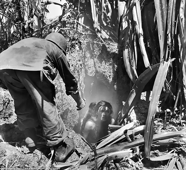 Un marine americano ayudando a salir de un agujero a una mujer de una de las islas del Pacfico que sufrieron en la WWII