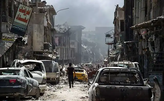 A-man-walks-by-destroyed-vehicles-in-a-street-in-the-Old-City-of-Mosul-on-July-2-2017.-AFP