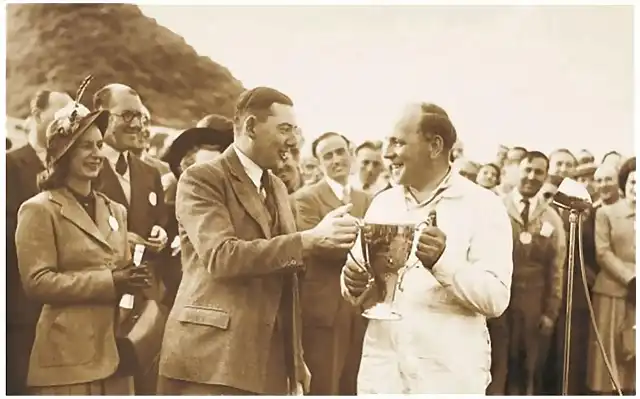 Dennis Perry, a director of the Kemsley Press, hands the winner's trophy for Goodwood's Formula One race to Reg Parnell