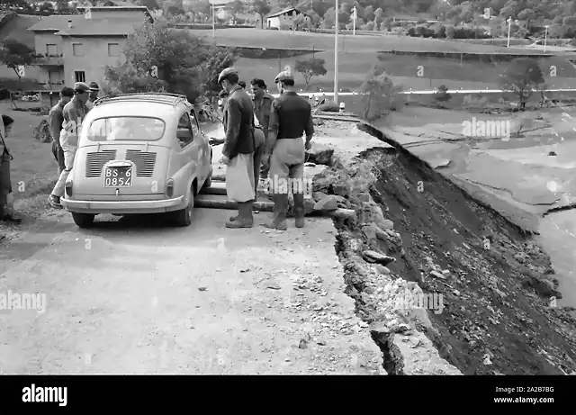 los-hombres-dejan-un-fiat-600-coche-en-carretera-rota-esta-carretera-fue-destruida-por-la-tormenta-en-italia-la-tormenta-devasto-las-ciudades-de-loveno-valcamonica-y-boario-terme-en-la-provincia-de-brescia-en-lombardia-2a2b7bg